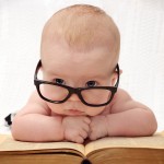 close-up of adorable baby in glasses lying on an old book and light background