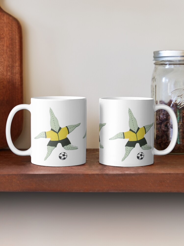 Two coffee mugs on a timber shelf with green starfish playing soccer printed on them